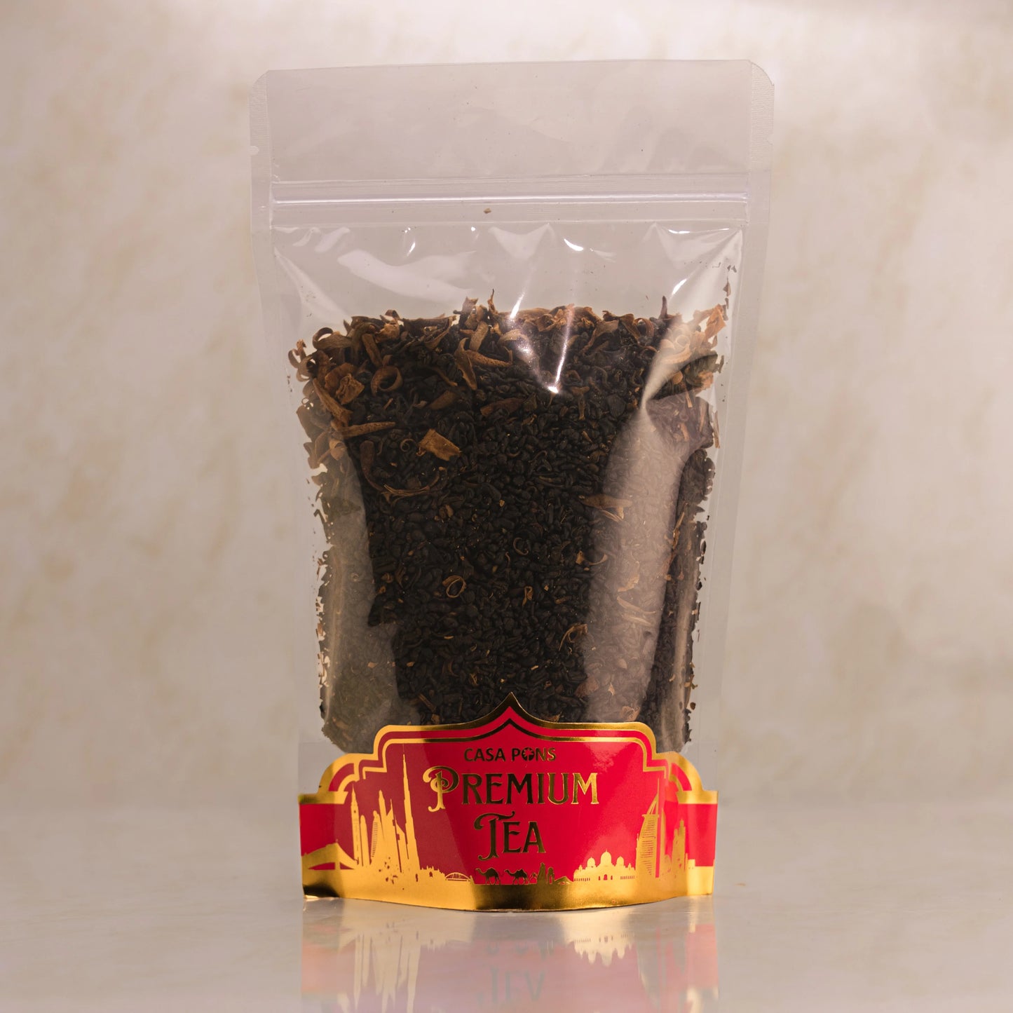 Clear plastic bag with black tea leaves and a red and gold label on a beige background