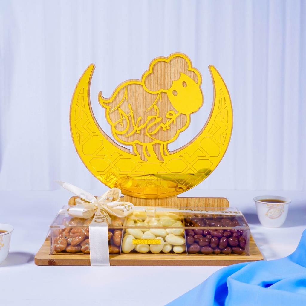 Decorative glass dish with sheep design on a crescent moon, placed on a wooden board with snacks.