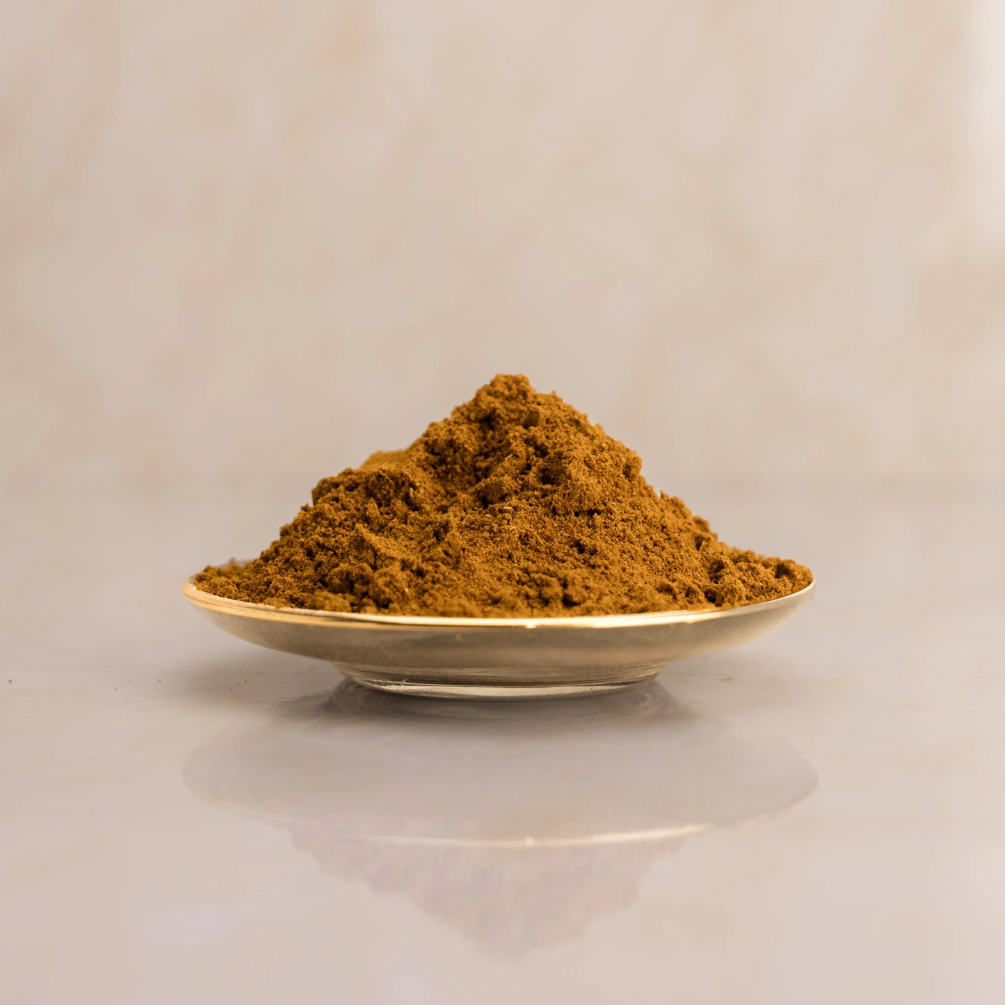 Brown powder of Kabsa in a gold spoon on a light beige background