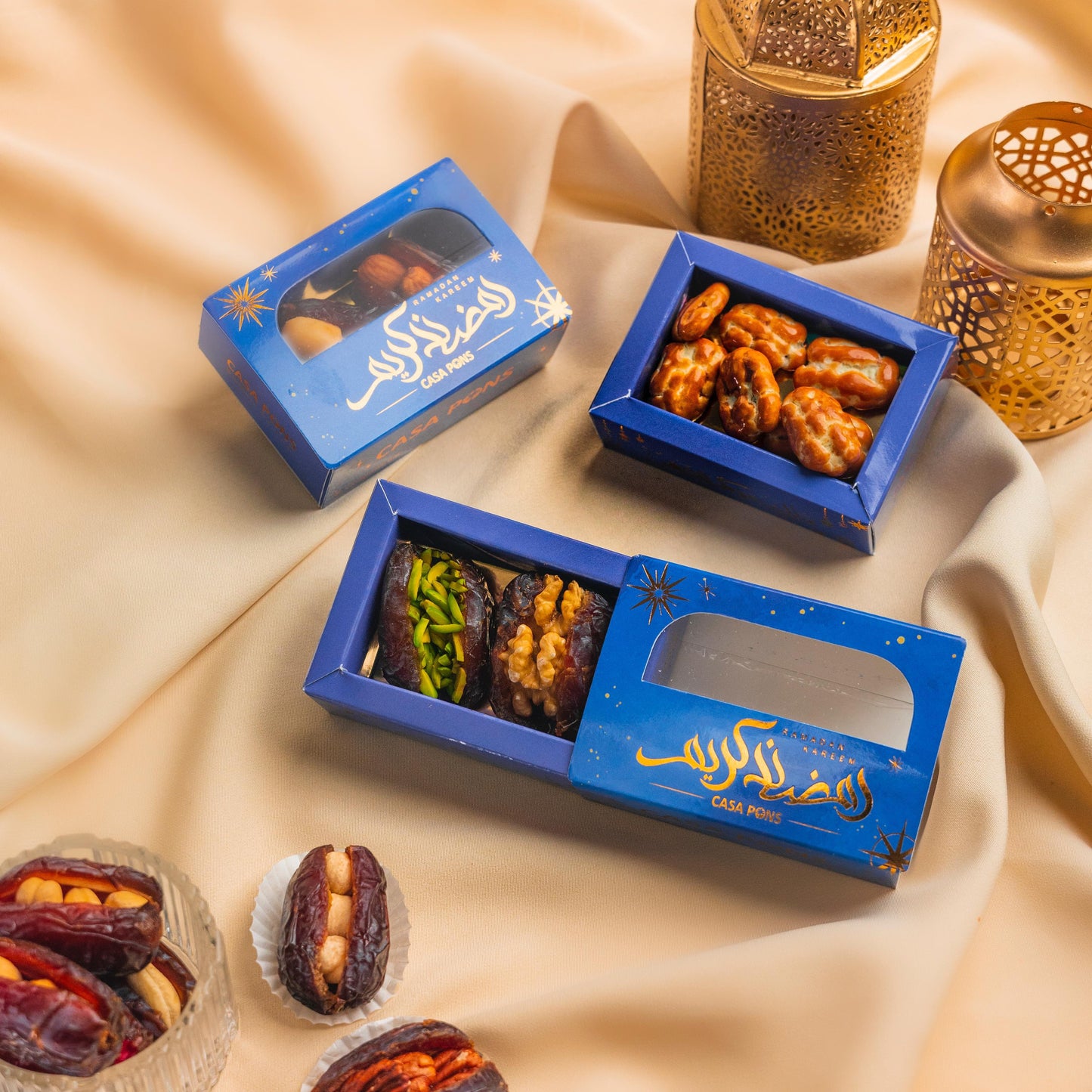 Three blue boxes of dried fruits and nuts on a beige fabric background with decorative lanterns.