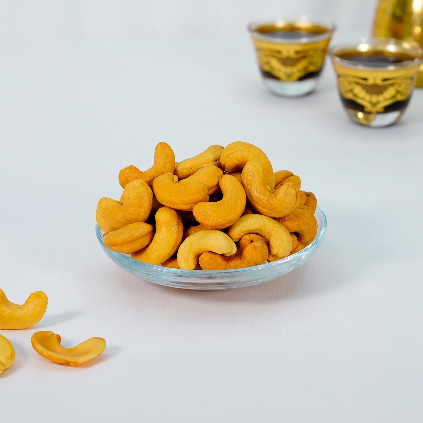 A glass bowl filled with cashew nuts on a table, with blurred objects in the background that might be glasses for drinking.