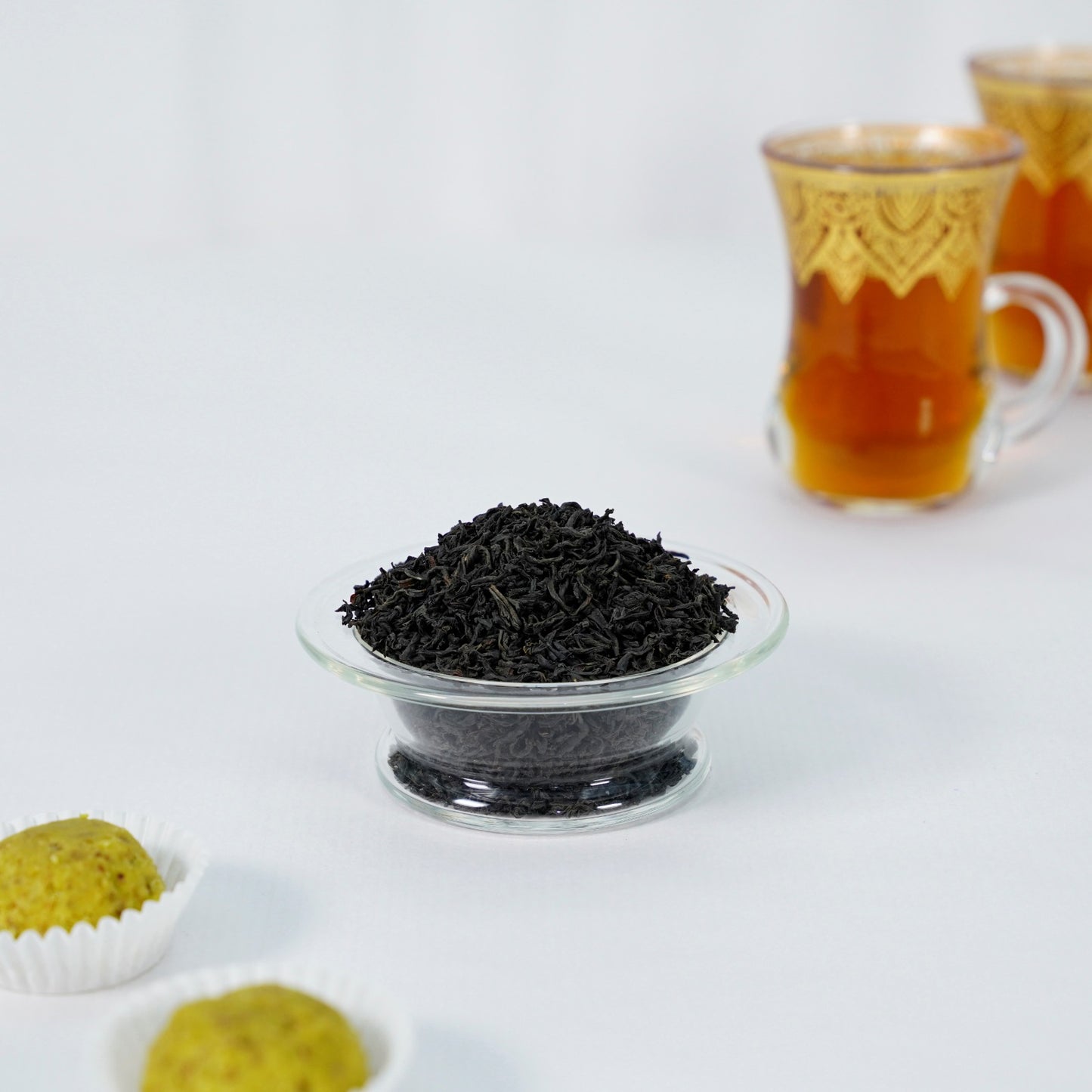 Black tea leaves in a glass bowl with a cup of tea in the background