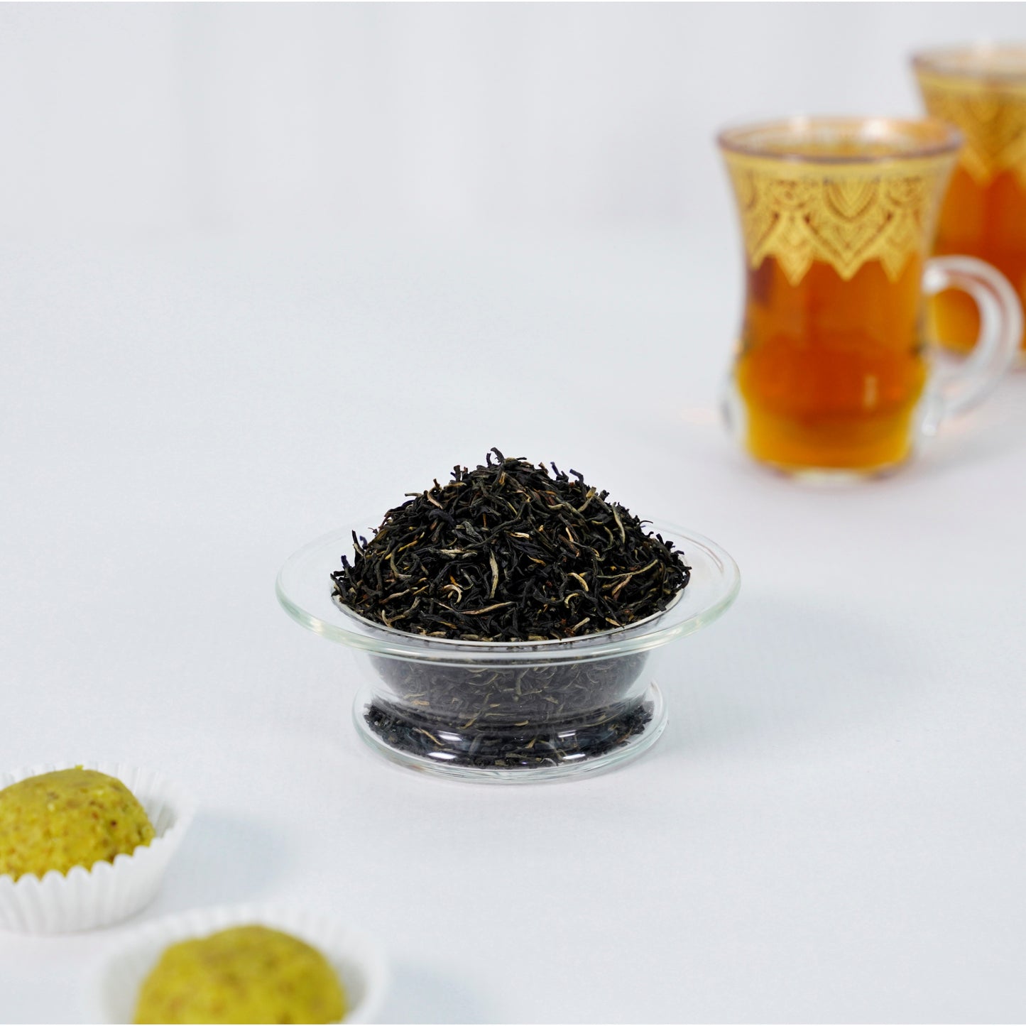 Tea leaves in a glass bowl with tea cups in the background