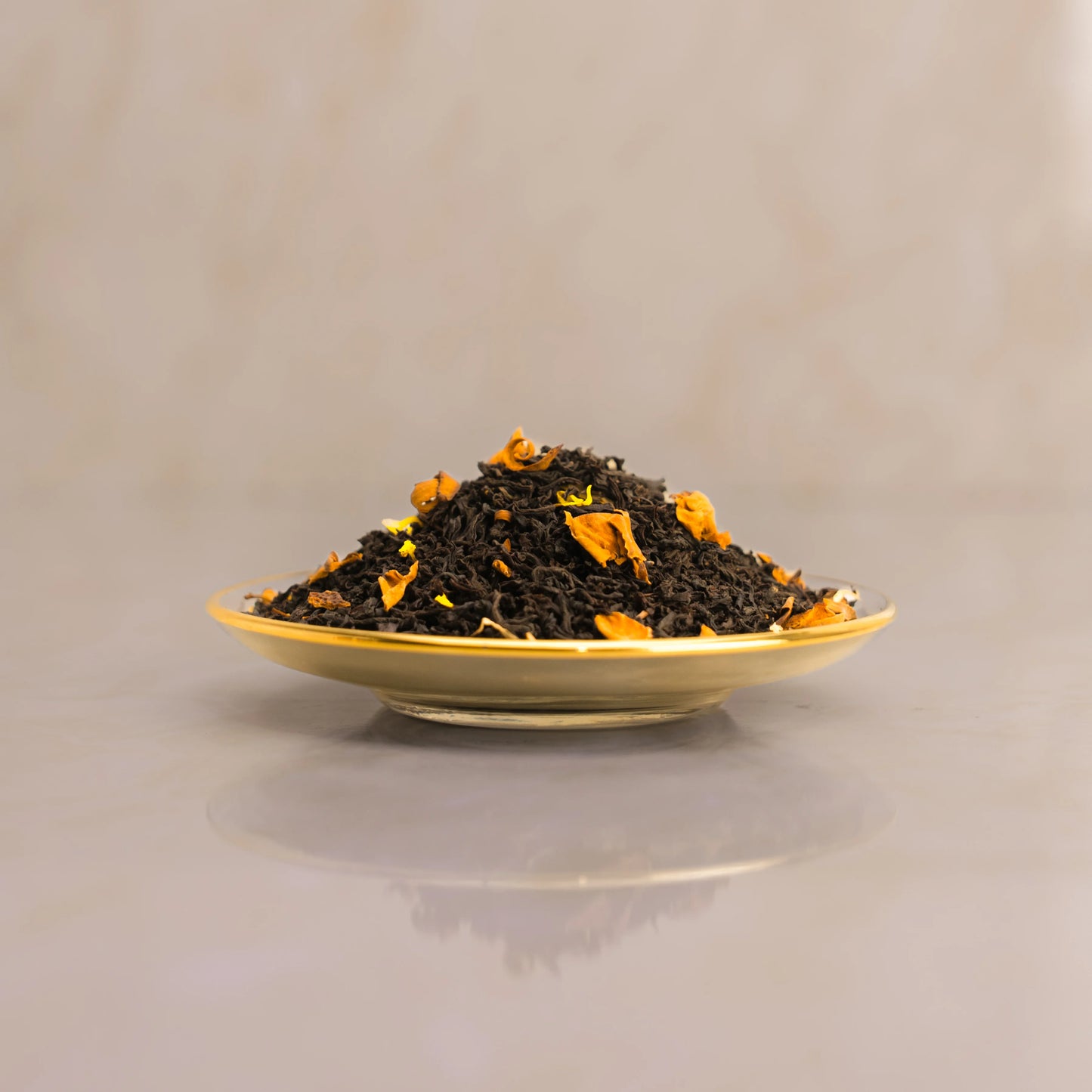 Dry black tea leaves with orange pieces on a gold plate against a beige background