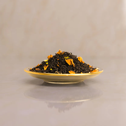 Dry black tea leaves with orange pieces on a gold plate against a beige background