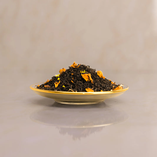 Dry black tea leaves with orange pieces on a gold plate against a beige background