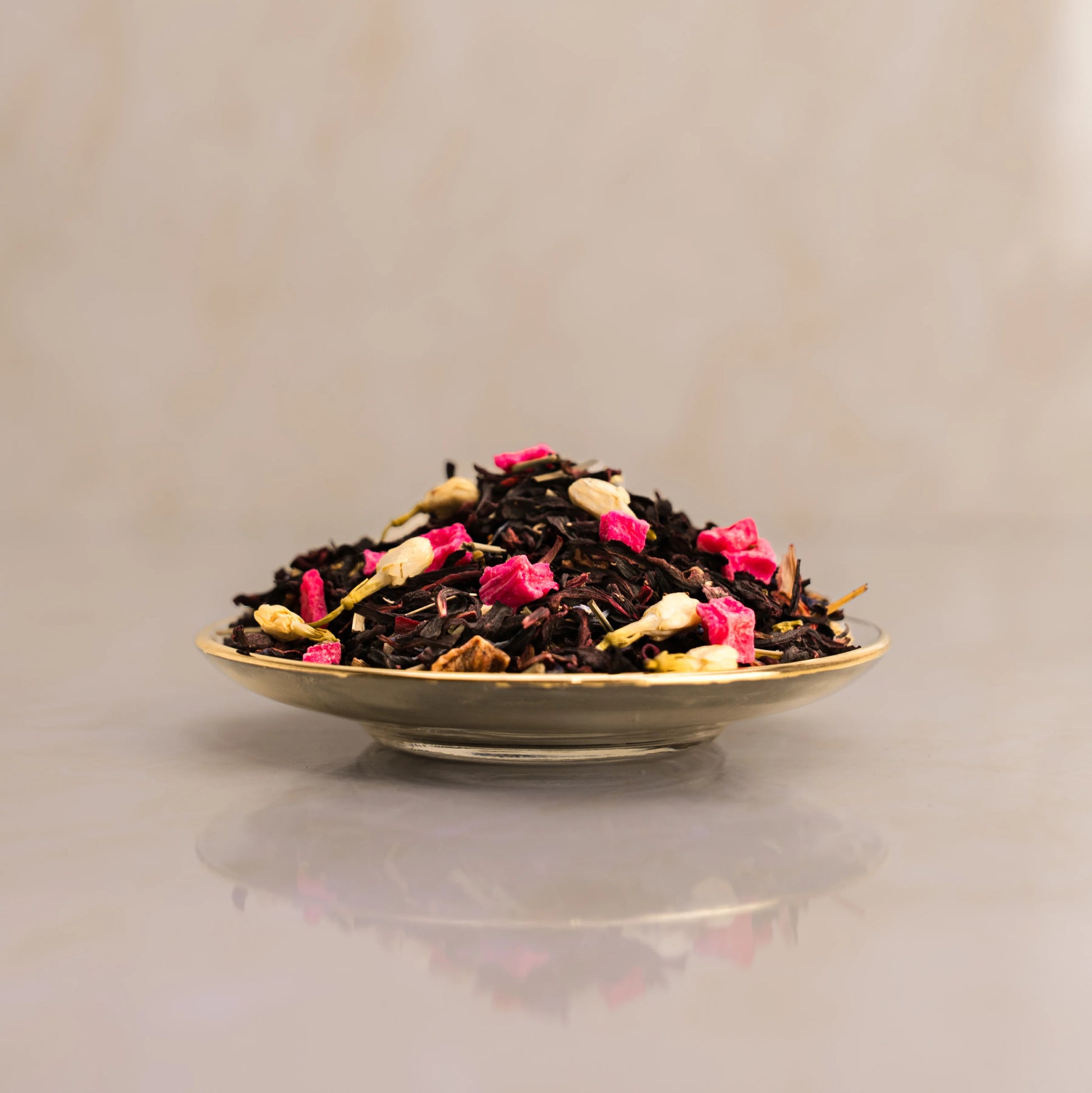 Tea leaves with pink flowers on a reflective surface with a neutral background