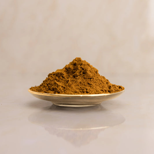 Brown powder of Kabsa in a gold spoon on a light beige background