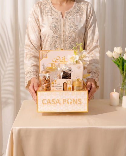 Person holding a 'Casa Pons' gift box with a white tablecloth and flowers in the background