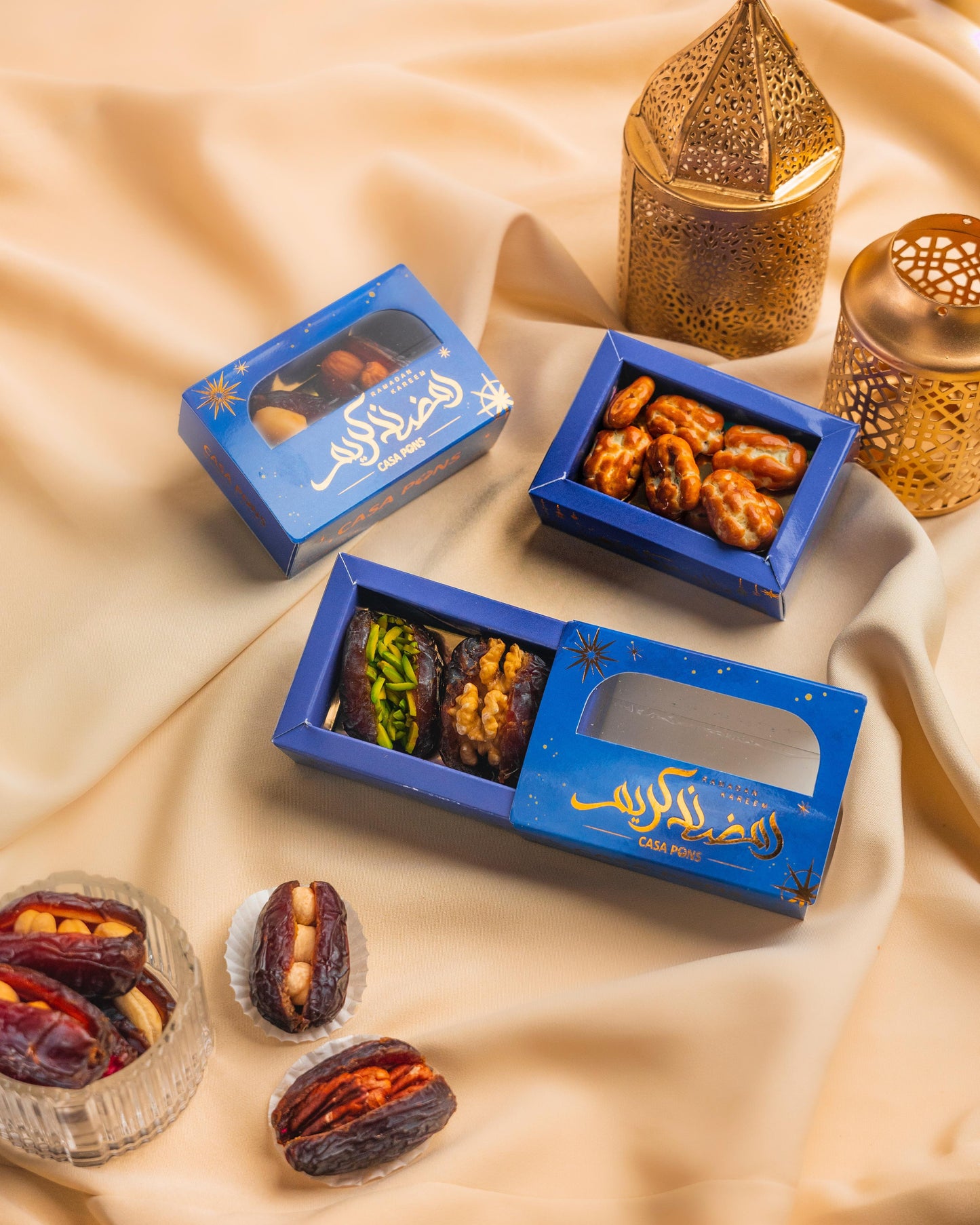 Three blue boxes of dried fruits and nuts on a beige fabric background with decorative lanterns.