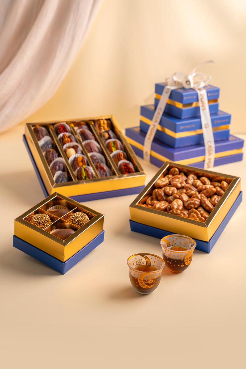 Assorted snacks in blue and gold gift boxes on a beige surface.