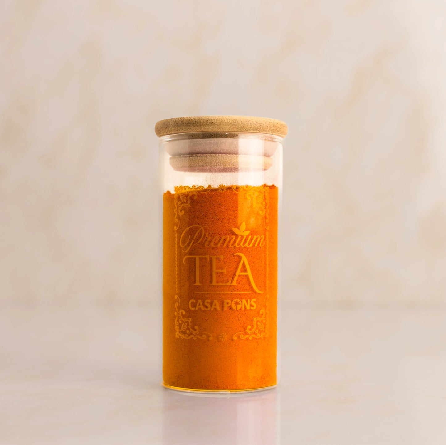 Glass jar with wooden lid containing tea, labeled 'Premium Tea Casa Pons' on a beige background.