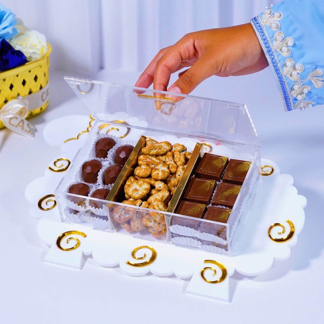 Clear decorative box with chocolates and nuts on a white surface