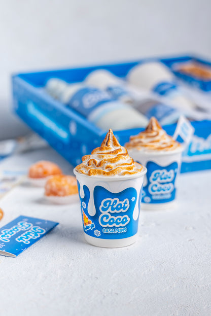 Two cups of Hot Cocoa with whipped cream on a white surface with a blue tray in the background.