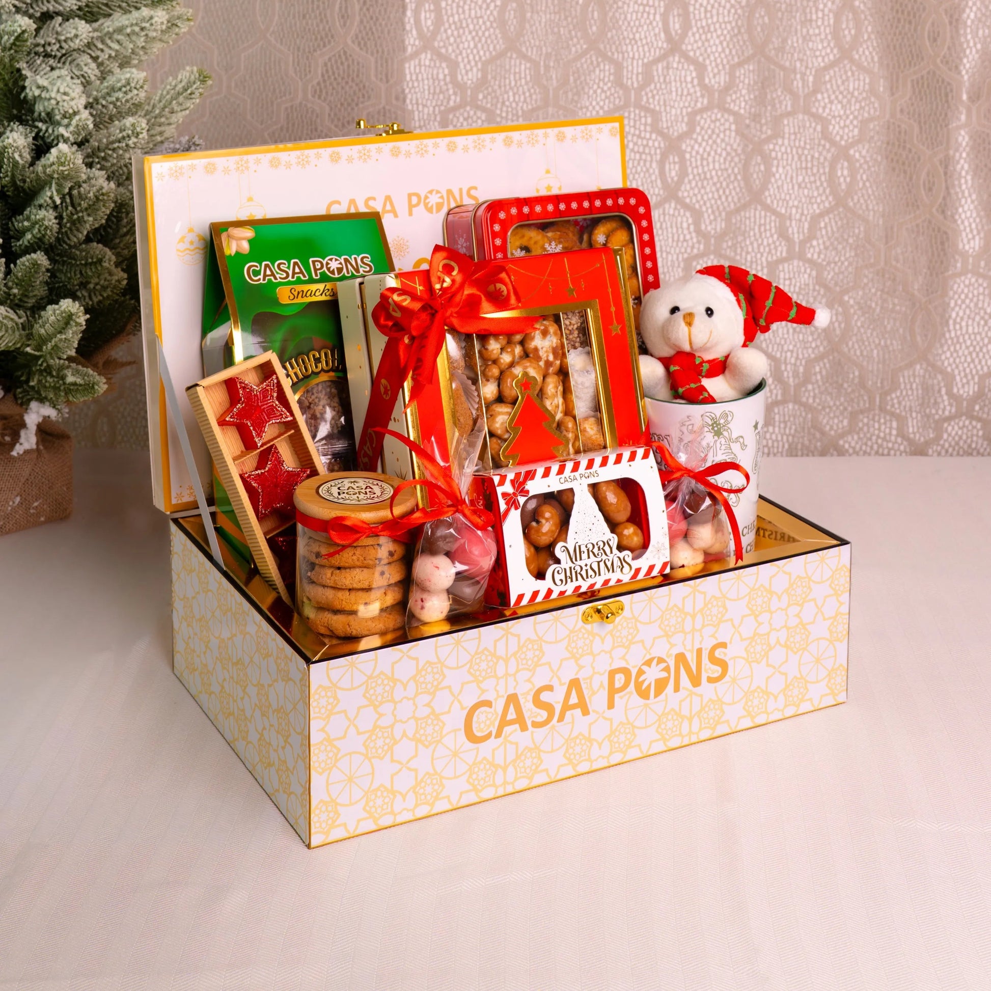 Gift box with various items including a teddy bear, cookies, and a candy bar, branded 'Casa Pons', on a neutral background.