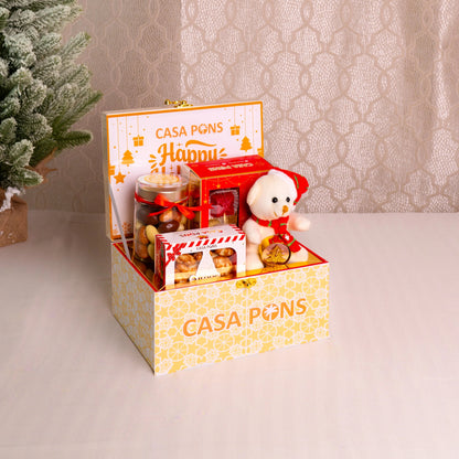 Gift box with 'Casa Pons' branding containing a teddy bear and various items on a neutral background.