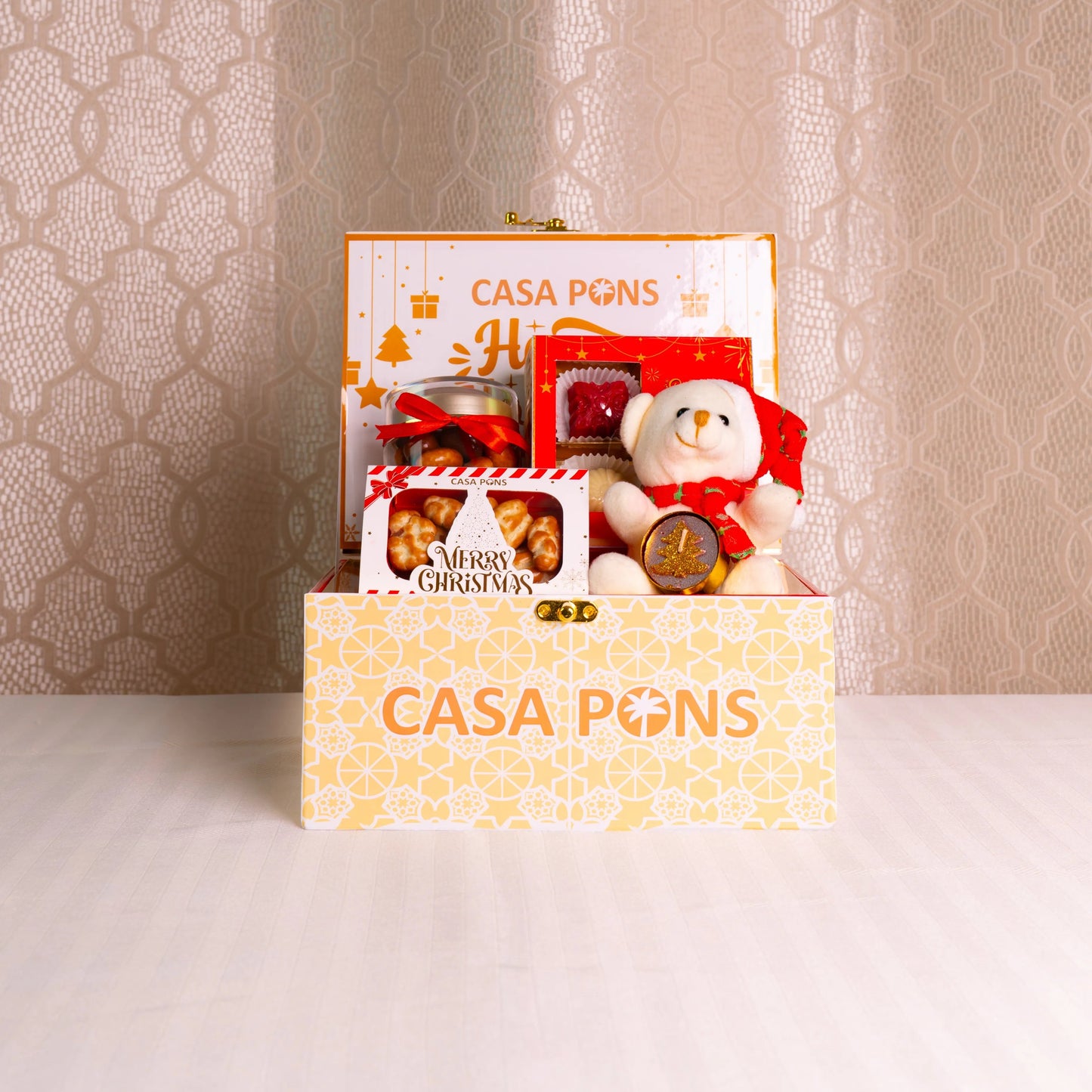 Gift box with a teddy bear and other items on a textured surface with a patterned wall background.